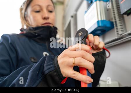 Woman using a crimping tool on an electrical wire, focusing on the installation process Stock Photo