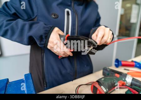 Person's hands using a crimping tool to attach a connector to a red electrical wire Stock Photo