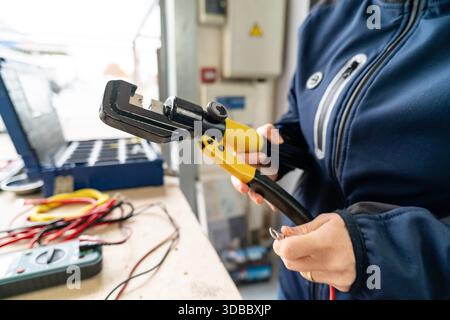 Technician holding hydraulic crimping tool and wire terminal for electrical connection Stock Photo