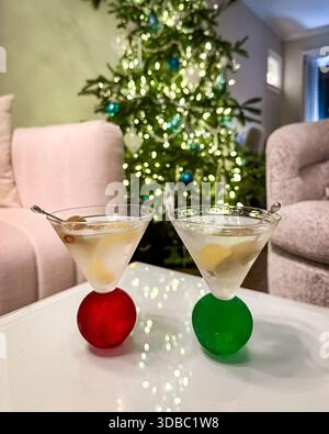 Two festive martini cocktails in red and green stem glasses, placed on a glass table with a softly glowing Christmas tree in the background. Stock Photo