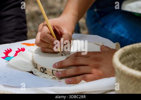Close-up of hands designing a pattern with a pencil on embroidery fabric with a nearby traditional Mexican floral design. Stock Photo