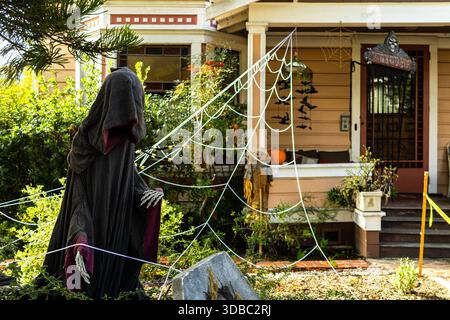 Spooky Halloween decorations in a front yard with a skeletal hooded ghoul gesturing towards a grave stone and fake spider webs covering the porch Stock Photo