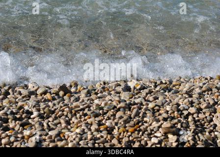 A slight foamy wave is crashing the shore over the pebbles on an Adriatic seaside Stock Photo