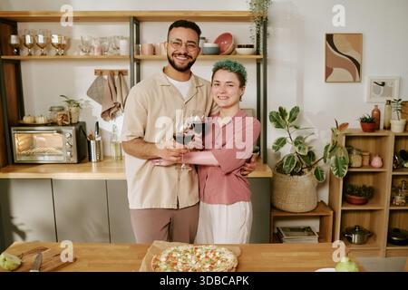 Young Multiethnic Couple Smiling and Toasting Wine Glasses in Kitchen Stock Photo