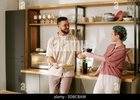 Young Man and Young Woman Toasting Wine in Kitchen Stock Photo