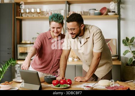 Young Woman and Young Man Cooking Together Using Tablet in Kitchen Stock Photo