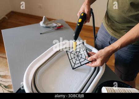 Close-up of cleaning service employee using steam cleaner to clean air humidifier filter in basin at home, ensuring regular maintenance for Stock Photo