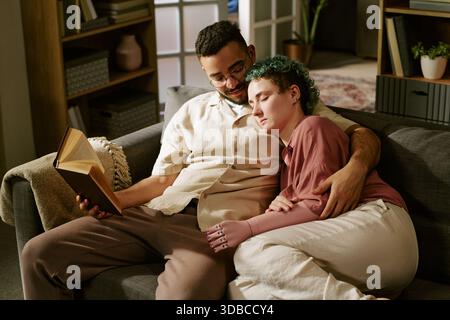 Young Woman with Prosthetic Arm Resting on Young Man Reading Book Stock Photo