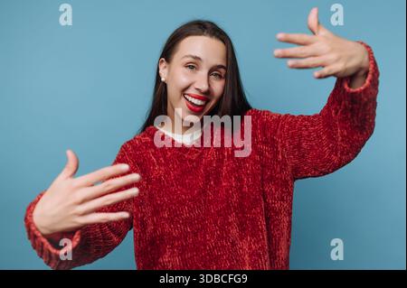 A woman shows happiness by laughing and using her hands while wearing a red sweater in front of a blue wall. This moment captures her energy and spiri Stock Photo