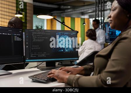 Software developer in office automating repetitive tasks using AI scripts on PC. African american woman uses artificial intelligence technology on computer to speed up feature implementation Stock Photo
