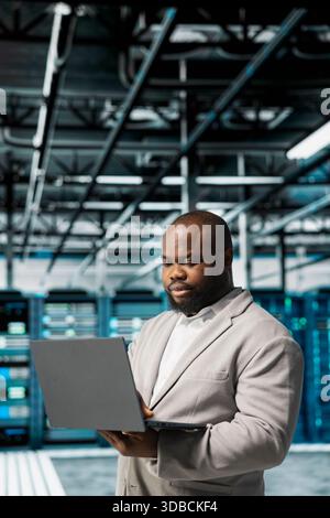 Server room IT specialist doing gear scans, fixing network issues affecting rigs performance. Data center engineer runs system diagnostic tests on notebook, tracking resource utilization Stock Photo