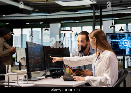 Friendly team leader mentor explaining young software engineer how to use AI tech. Joyous supervisor guiding office newcomer through AI tool integration, mentoring her on using neural networks APIs Stock Photo