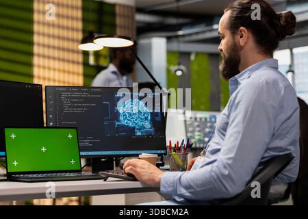 Technician using green screen tablet to code AI algorithms debugging software issues in tech startup office. Man at work using chroma key device, improving system stability Stock Photo