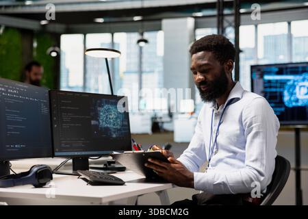 Engineer in modern office using AI tools to automate routine coding tasks, reviewing manual instructions. IT expert reading clipboard notes, using artificial intelligence to accelerate development Stock Photo
