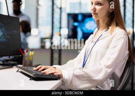 Jolly junior dev in office using AI on computer to streamline app development. Young female engineer at desk using PC to run debugging programs with machine learning technology Stock Photo