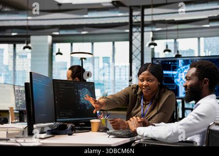 Happy team leader oversees developer in wheelchair using AI automation, refining algorithms. Joyous supervisor satisfied by progress done by programmer with paraplegia using artificial intelligence Stock Photo