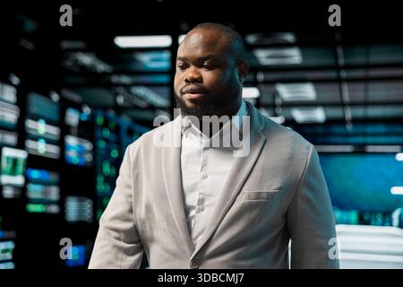 Admin working in data center, overseeing infrastructure mainframes. African american man walking in server farm workplace hosting websites and delivering web content to online customers Stock Photo