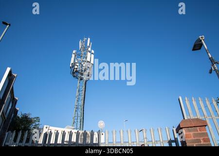 A tall mobile phone mast captured against a clear blue sky, showing modern cellular network infrastructure and telecom equipment. Stock Photo
