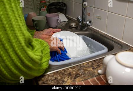 Older person washing dishes by hand in a sink, a common household chore in a typical kitchen setting Stock Photo