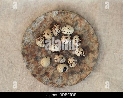 Minimalist flat lay still life of quail eggs arranged on a rustic ceramic plate over natural linen fabric. Earthy textures, muted colors, and simple c Stock Photo