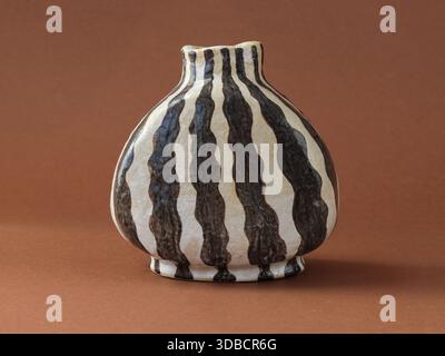 Studio still life of a handbuilt ceramic vase with expressive black striped pattern on neutral clay surface. Minimalist composition and earthy tones h Stock Photo
