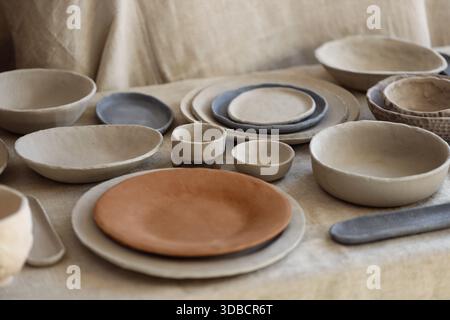 Assortment of handmade clay bowls and plates arranged on textured fabric. Studio photograph showing unglazed ceramic tableware with natural tones and Stock Photo