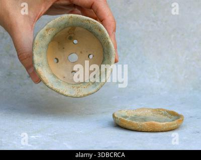 Minimalist still life of a small handmade ceramic succulent pot with drainage holes and matching saucer, held in hand. Natural textures and muted tone Stock Photo