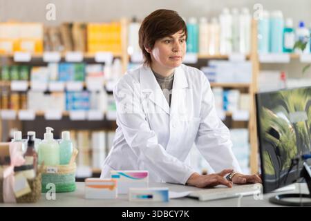 Female pharmacist working on computer at pharmacy counter Stock Photo
