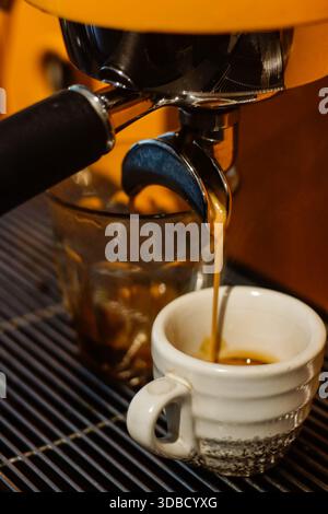 Fresh espresso coffee pouring from professional coffee machine into clear glass, close up barista equipment Stock Photo