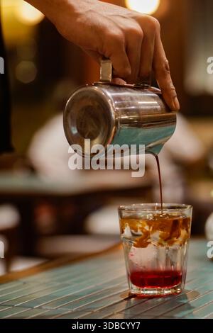 Barista pouring freshly brewed coffee into glass, coffee preparation process in café with warm lighting Stock Photo