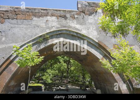 View of an old stone bridge structure against a wooded background on a sunny day, part of a three-arched bridge over the Kassagh from 1664, Ashtarak, Stock Photo