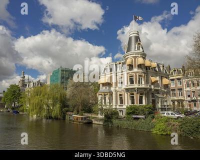 Majestic buildings on the canal surrounded by blooming spring trees under a cloudy sky, Amsterdam, the Netherlands Stock Photo