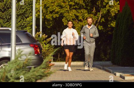 Couple running side by side on sunny park sidewalk, casual morning workout Stock Photo