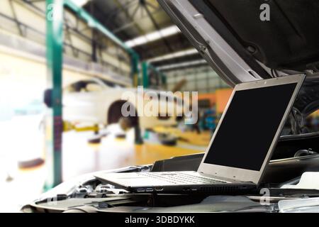 Digital Car Diagnostics, A laptop with blank screen sits on a car engine in a modern auto repair shop, displaying diagnostic data while a vehicle is e Stock Photo