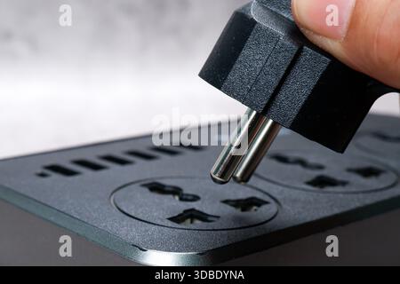 European Power Plug Connection, Close-up of a hand inserting a black European Type C power plug into a multi-socket extension lead, highlighting elect Stock Photo