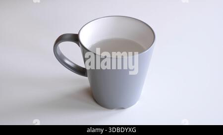 A grey ceramic mug with water stands on a white table, side and top view. Fresh water as a morning ritual. One object in the center of frame close-up Stock Photo
