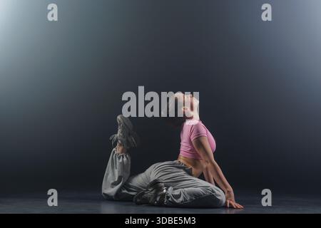 Full length side view of young woman practicing jazz funk hip hop floor backbend stretch for flexibility and mobility in haze Stock Photo