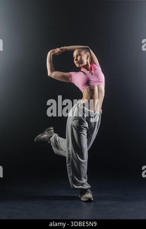Full length portrait of young woman balancing in jazz funk hip hop pose in studio spotlight for dance training and lesson promotion Stock Photo