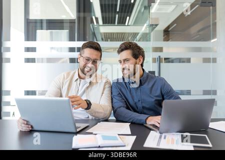 Two professional businessmen collaborating and discussing work using a laptop in a modern office meeting room, focusing on data and reports for successful teamwork Stock Photo