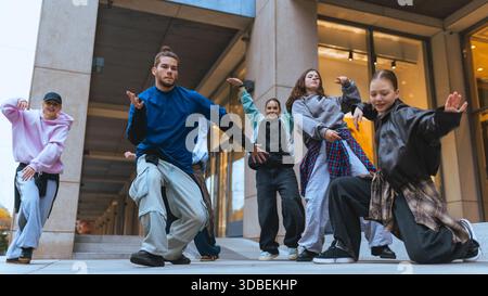 Group of street dancers practicing expressive moves in city plaza setting. Stock Photo