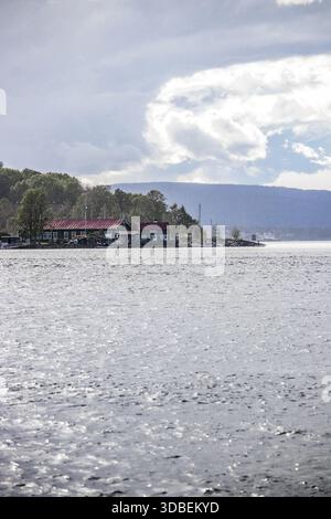 View of tranquil waters reflecting the sky, with a building nestled among trees on the distant shore, creating a serene contrast against the mountains Stock Photo