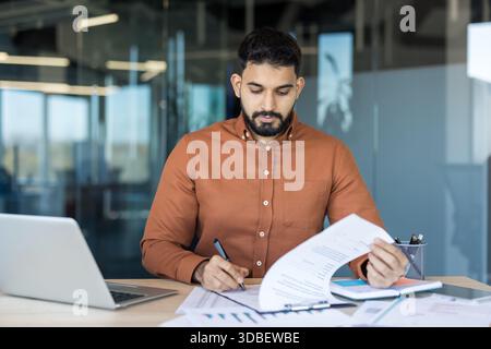 Indian business man working at a modern office desk, reviewing and signing paperwork, managing documents with focus and professionalism, representing business administration and corporate workflow Stock Photo