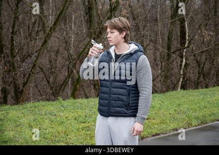 Athlete and sporty caucasian man drinking water from bottle at public park after workout. Outdoors. Water balance. Young Man Training Outdoors Stock Photo