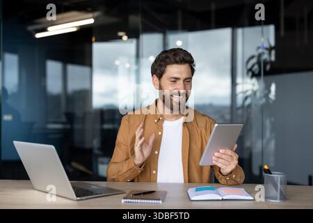 Man smiling during an online video call using a digital tablet at his office desk, actively communicating and participating in a remote virtual meeting Stock Photo
