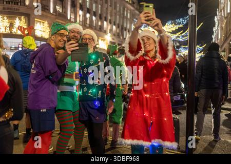 London, UK, December 13, 2025, Group of runners in christmas-themed costumes taking a selfie on a city street at night Stock Photo