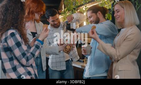 Group Caucasian friends eating cookies in office startup company smiling talking lunch break multiethnic business men women informal casual team Stock Photo