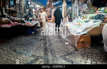 Istanbul, Turkey  - 8th December, 2025, Shoppers navigating a historic cobblestone alleyway lined with retail stalls and goods in a vibrant Turkish ba Stock Photo