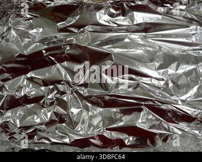 Crumpled aluminum foil with reflective metallic surface, strong highlights and deep shadows. Close-up. Copyspace. Stock Photo