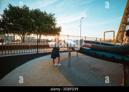 kids playing happily, children interact playfully on swing with sunset and silhouette Stock Photo