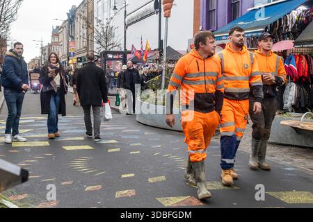 London, UK, December 13, 2025, Three construction workers in bright orange workwear walking on a busy city street Stock Photo